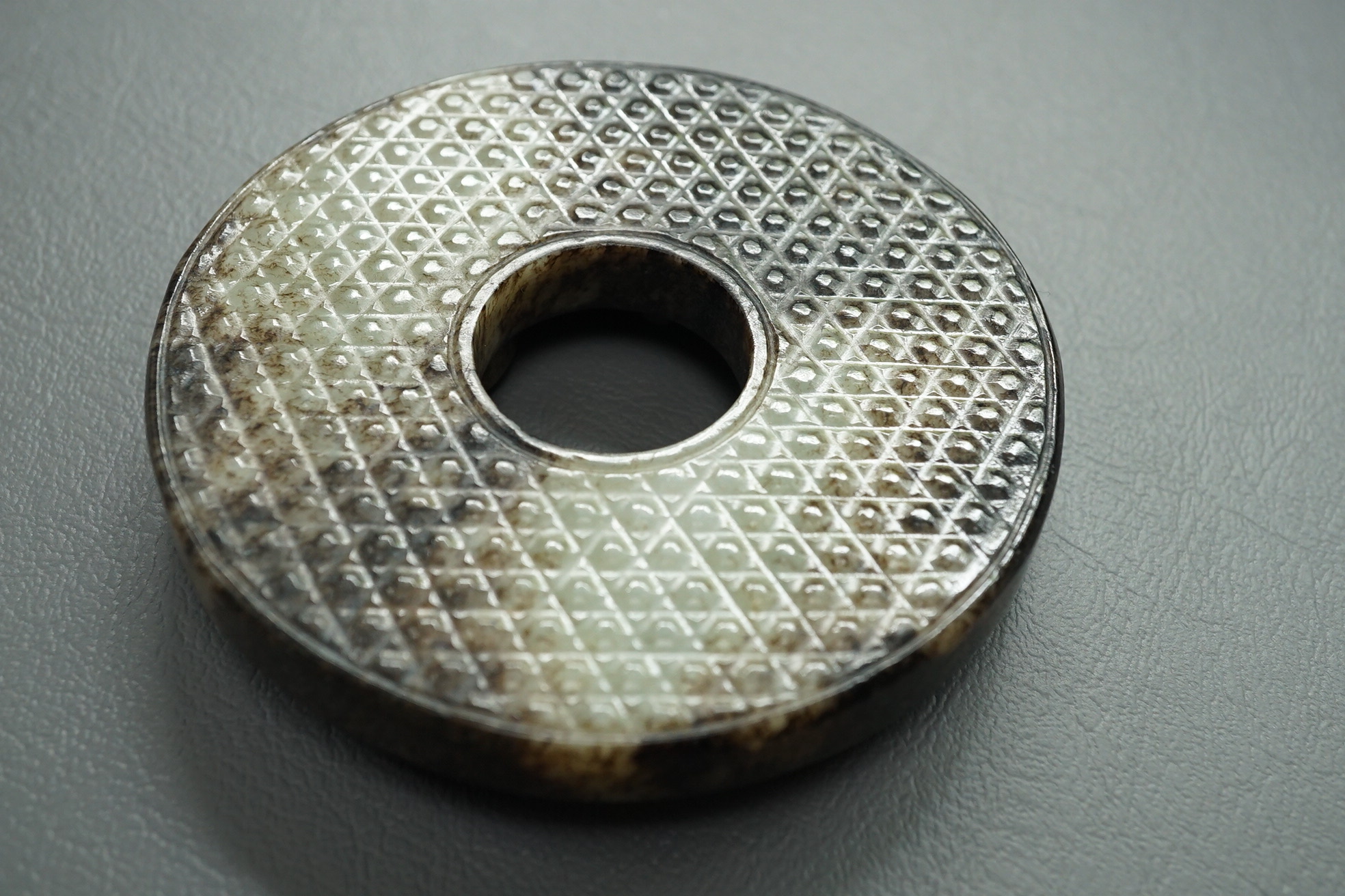 A Chinese pale celadon and black jade bi disc